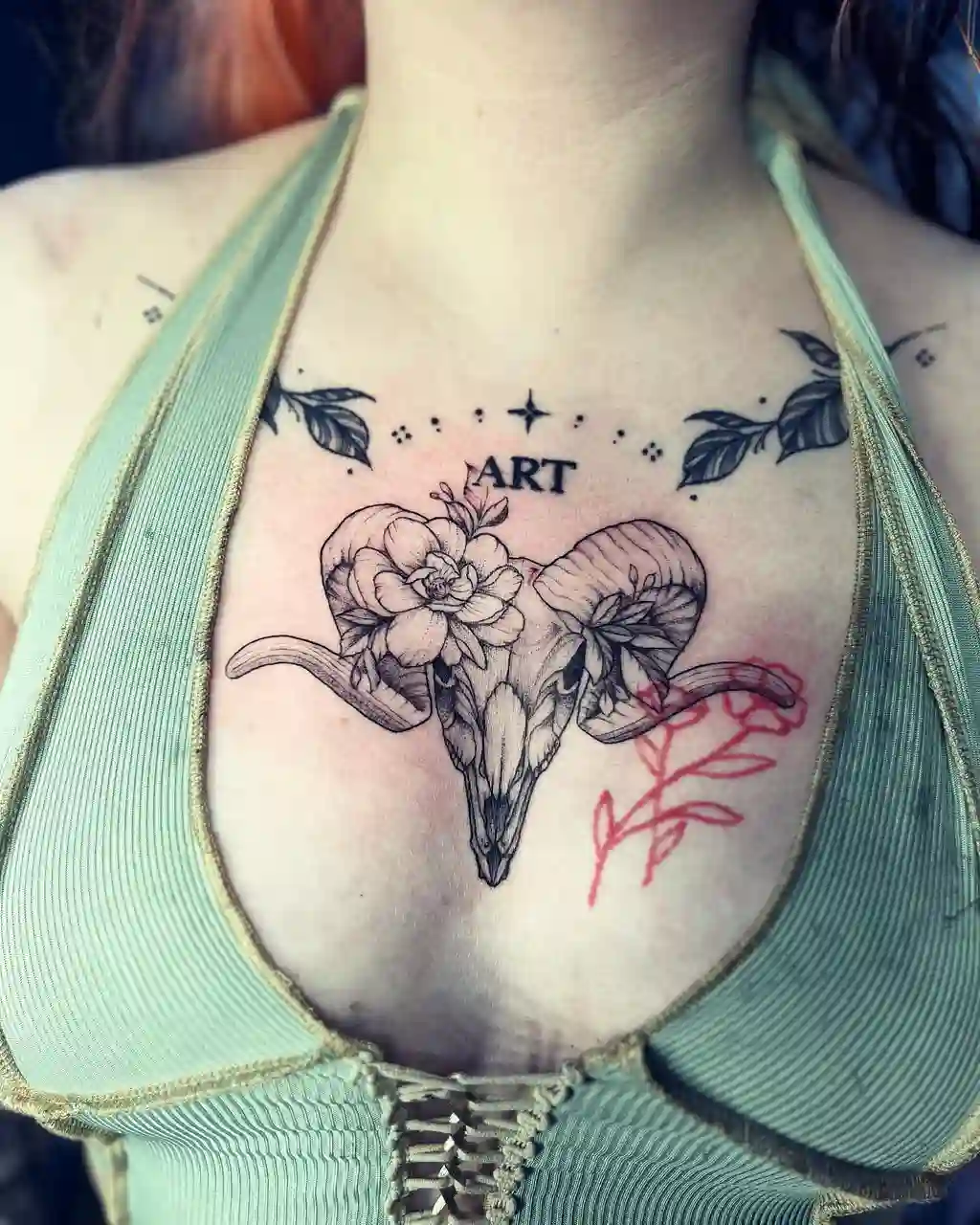 Chest Tattoo Female with Ram Skull, Flowers, and "ART" Text